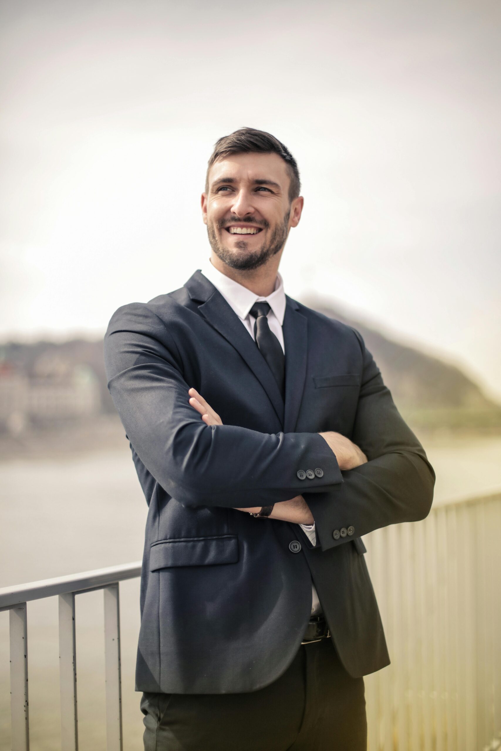 confident businessman in suit standing outdoors with crossed arms.